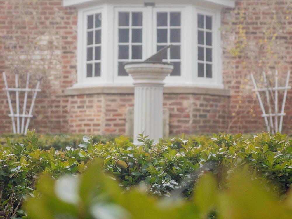 a sundial sits behind a hedge