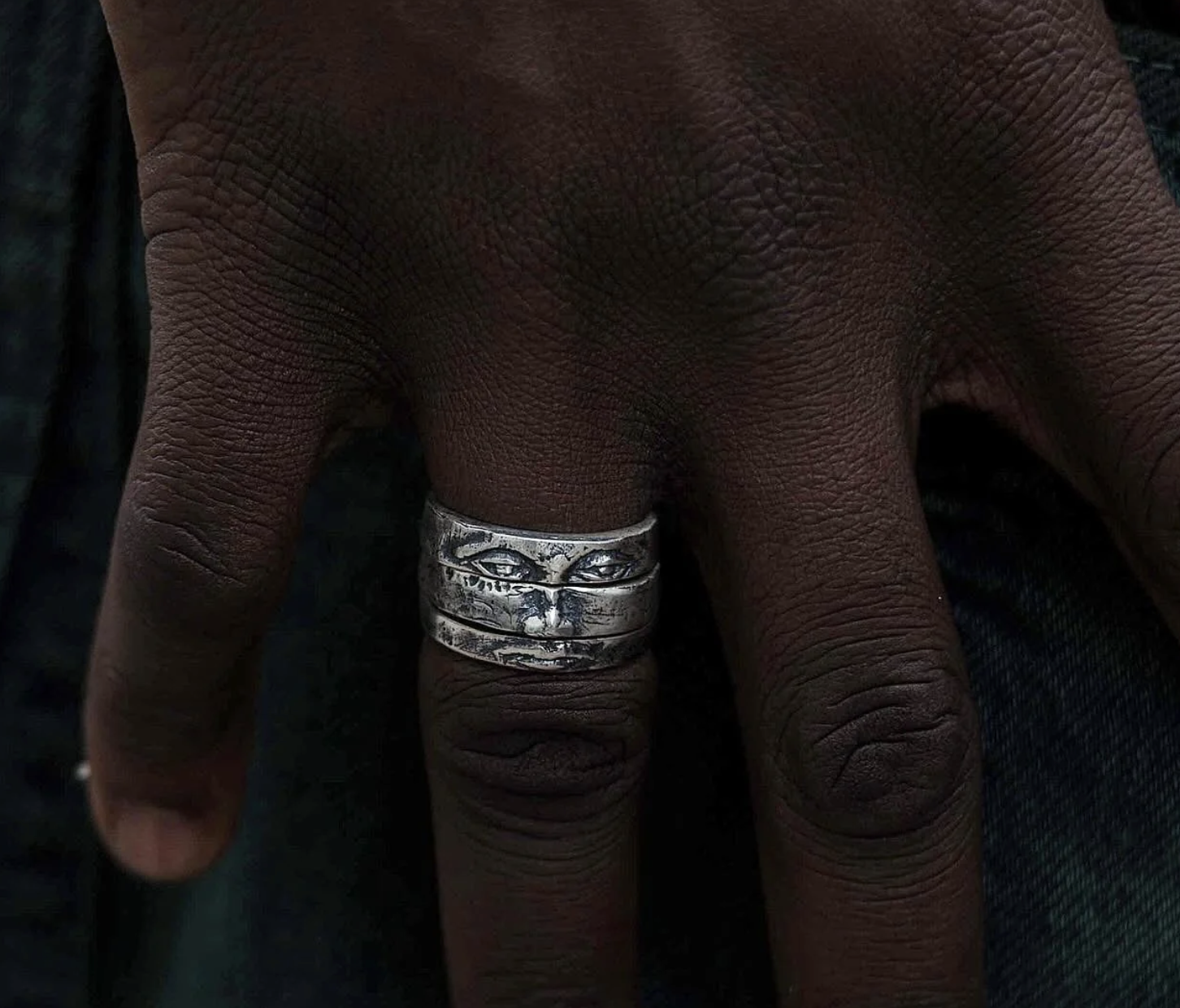A hand wearing a silver ring that looks like a face